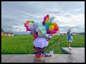 一位拿着雨伞 带着彩色气球站在稻田里的女人