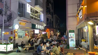许多人在城市的夜晚坐在餐馆外面的桌子旁。