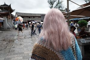 一位粉色头发的女士打着蓝色雨伞在雨中走街
