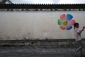 一位年轻女子抱着彩色气球走过一个有花的墙
