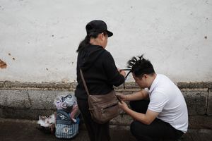 一位男子在人行道上跪着 旁边有一位女士和一只猫在纸袋里。