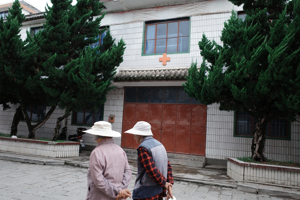 一位老人和一位女士戴着帽子走在一栋建筑前面的街道上。