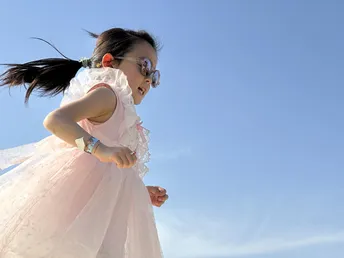 一位穿着白色连衣裙的年轻女孩在蓝天下沿着海滩奔跑