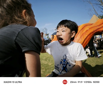 一个小男孩在公园里做鬼脸 背景中有一个女人和两个女人和一个年轻的孩子。