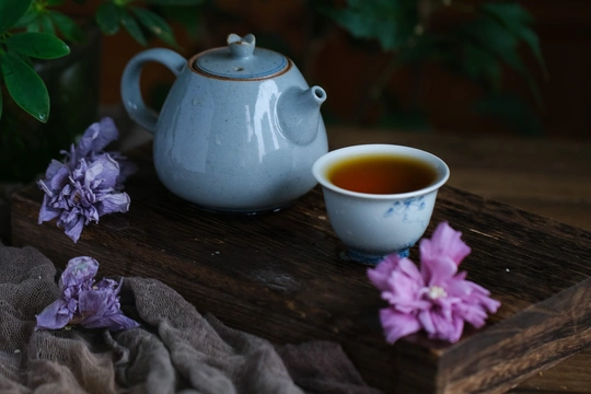 一个蓝色的茶壶和一杯茶放在一张开着紫色花朵的木桌上
