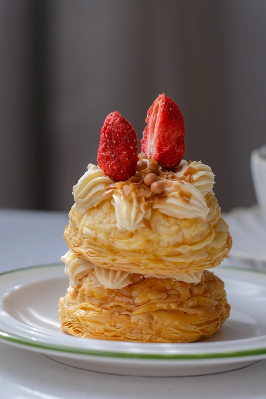 一堆薄煎饼 上面放着生奶油和一颗草莓 放在一个白色盘子里