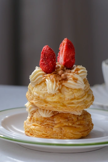 一堆薄煎饼 上面放着生奶油和一颗草莓 放在一个白色盘子里