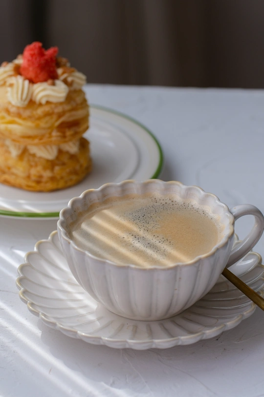 一杯放在白色盘子里的咖啡 配一把勺子和一些糕点