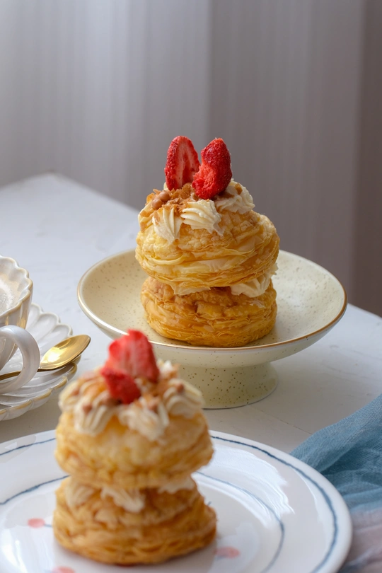 放在一杯茶旁边的一个白色盘子里的一叠煎饼 上面有树莓和奶油