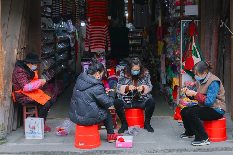 有些人戴着口罩坐在街道人行道上的一家商店外的红色桶旁边。