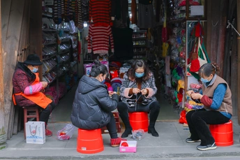有些人戴着口罩坐在街道人行道上的一家商店外的红色桶旁边。