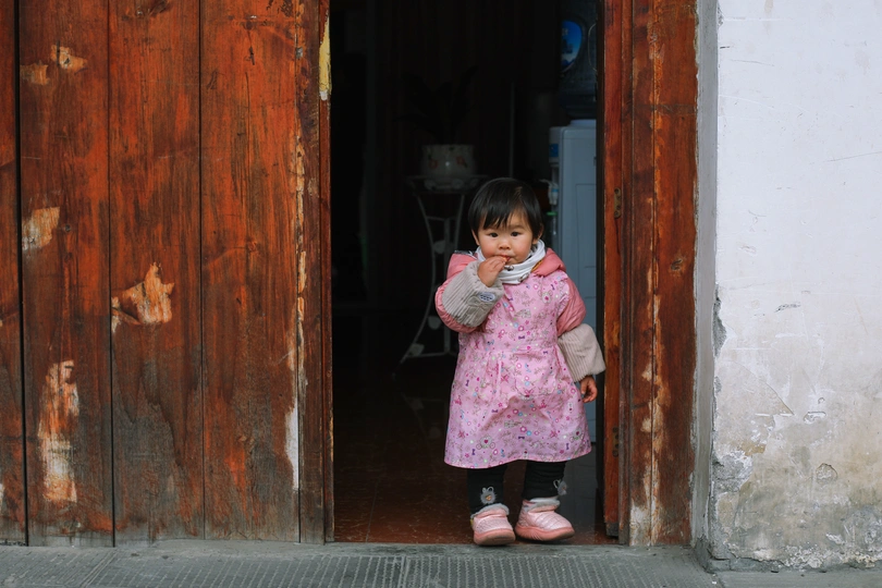 一个小女孩穿着粉红色裙子站在一扇木门前面