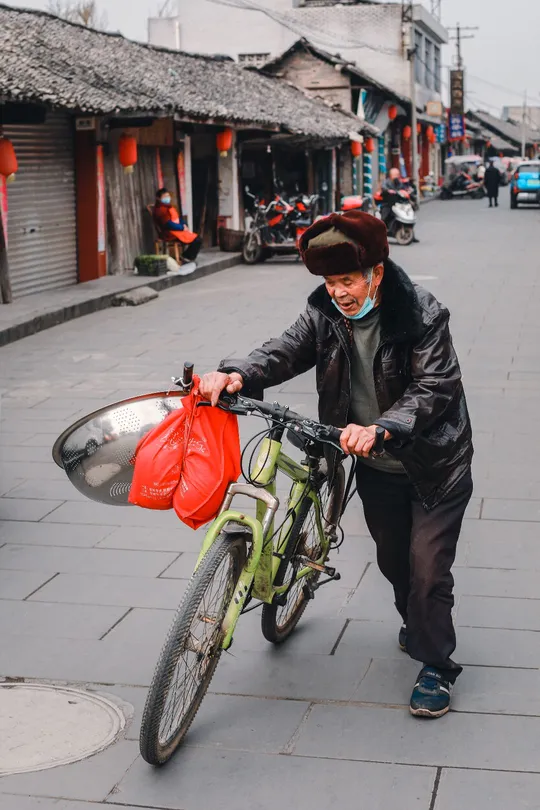 一个戴帽子老人推着自行车沿街走