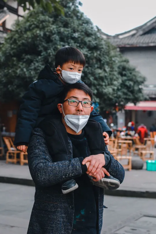 一个肩上背着孩子的男人和戴口罩的女人走在街上