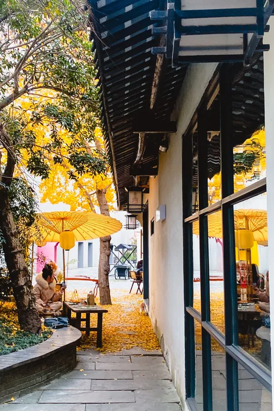 一位坐在黄色雨伞下的长凳上的女人 旁边是建筑物。