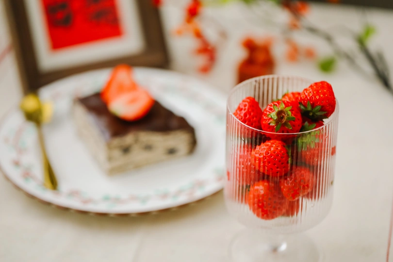 桌子上放着一小盘草莓 旁边放着一块蛋糕和一些框起来的图片。