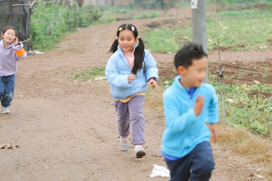 两个年轻女孩沿着土路跑下来 其他孩子在背景中玩耍。