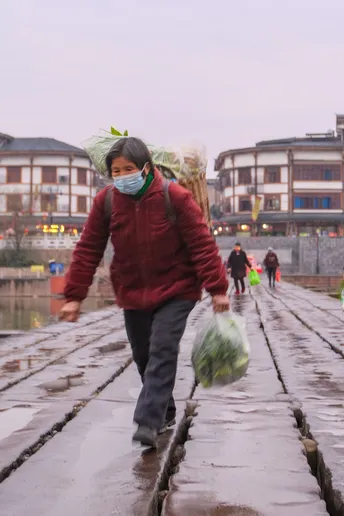 一个戴防护面罩的男子带着一个孩子 在雨中走在一个湿砖铺成的小径上 人们穿着雨衣。