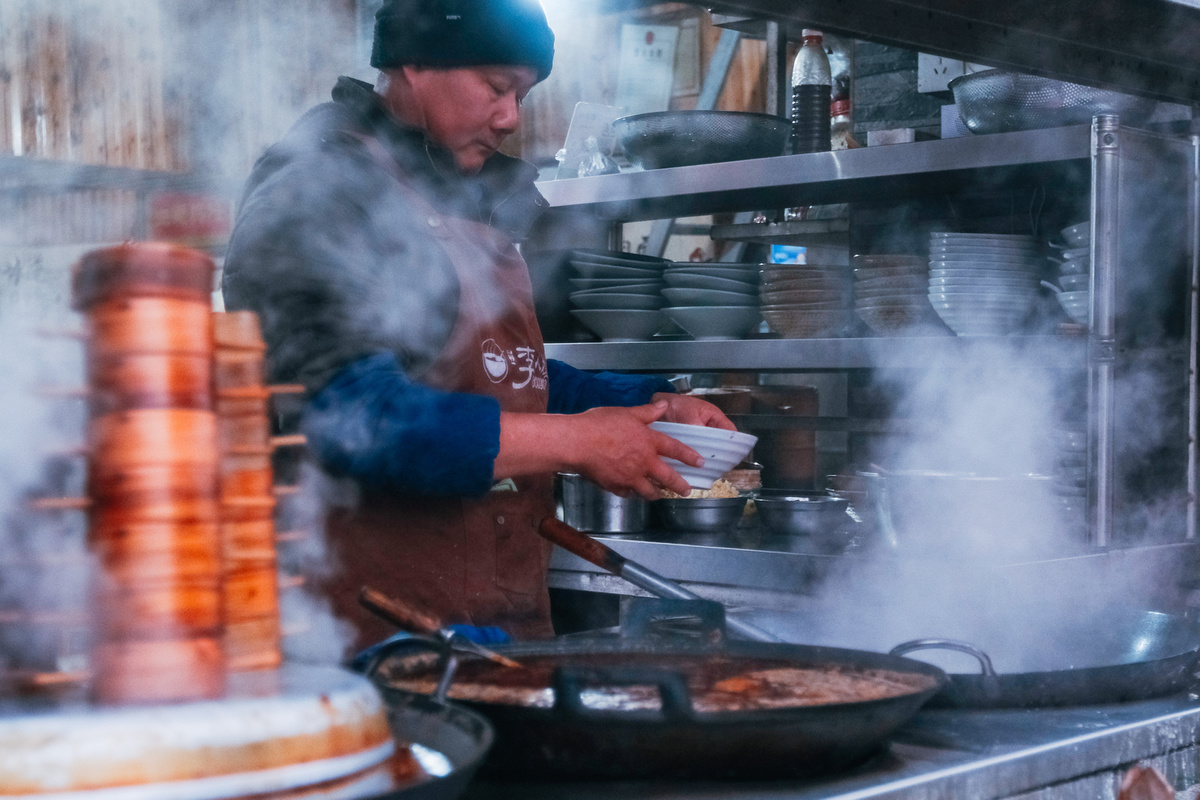 一个男人在餐馆的炉子上用大锅炖着一些食物。