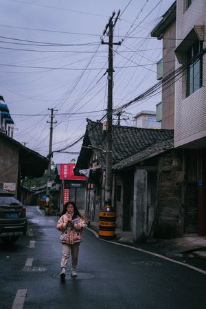 一个年轻女子打着伞走在一排建筑物旁边的小街上。