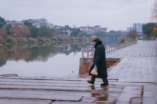 一个人带着雨伞和雨衣在雨中靠近水体行走