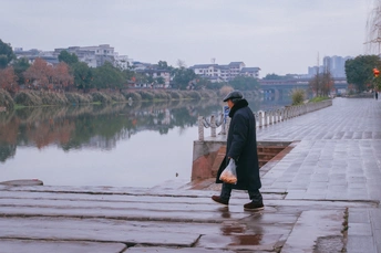 一个人带着雨伞和雨衣在雨中靠近水体行走