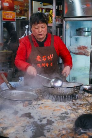 一个戴红围裙的妇女正在一口大锅中烹饪食物