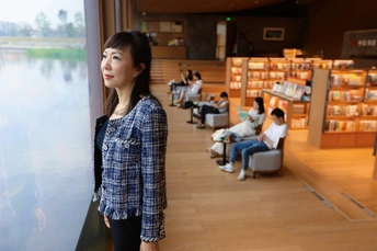 一个年轻女子站在书店里 透过窗户看着楼里的人们。