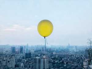 天空上飘着一个黄气球 位于一个大城市上。