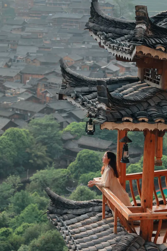 一位女性坐在阳台上 可以俯瞰到建筑的屋顶和背景中的城市。