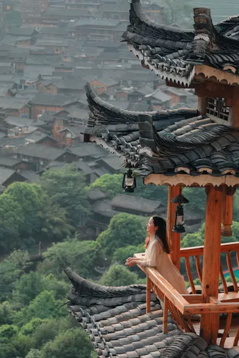一位女性坐在阳台上 可以俯瞰到建筑的屋顶和背景中的城市。