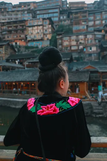 一位穿着和服的年轻女孩站在一座桥上 眺望着河对岸。