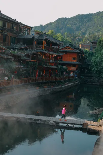 一位妇女走过一座村庄中的河流上的桥 背景是建筑物。