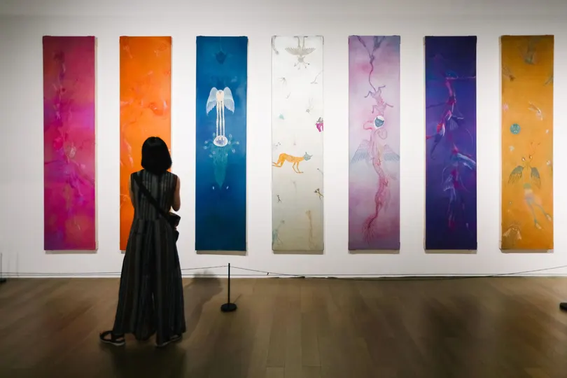 一个女性站在艺术画廊里 看着一幅色彩斑斓的画作墙。