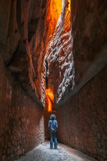 一位徒步者站在一个狭窄的山洞里 阳光透过墙壁照进来。