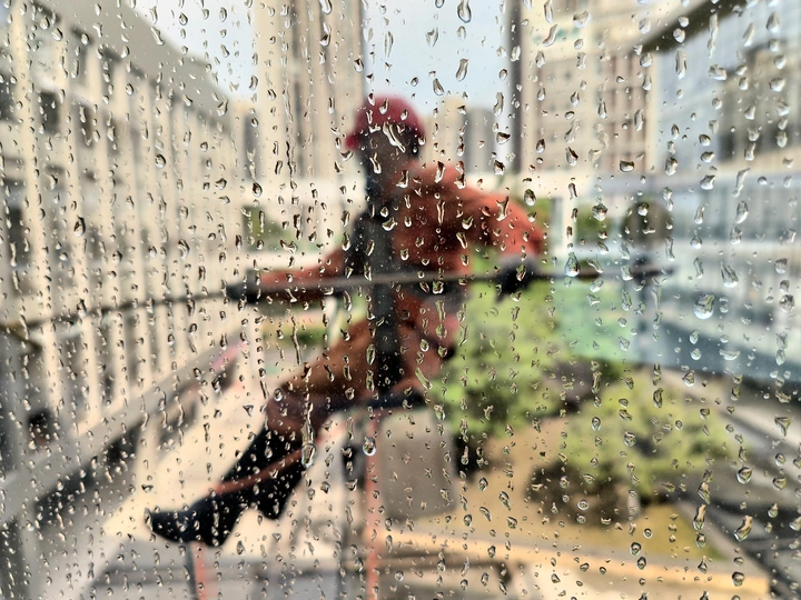 一位女士站在雨中 旁边是一位骑着自行车的男子 她正看着窗户。