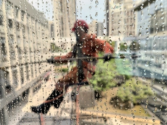 一位女士站在雨中 旁边是一位骑着自行车的男子 她正看着窗户。