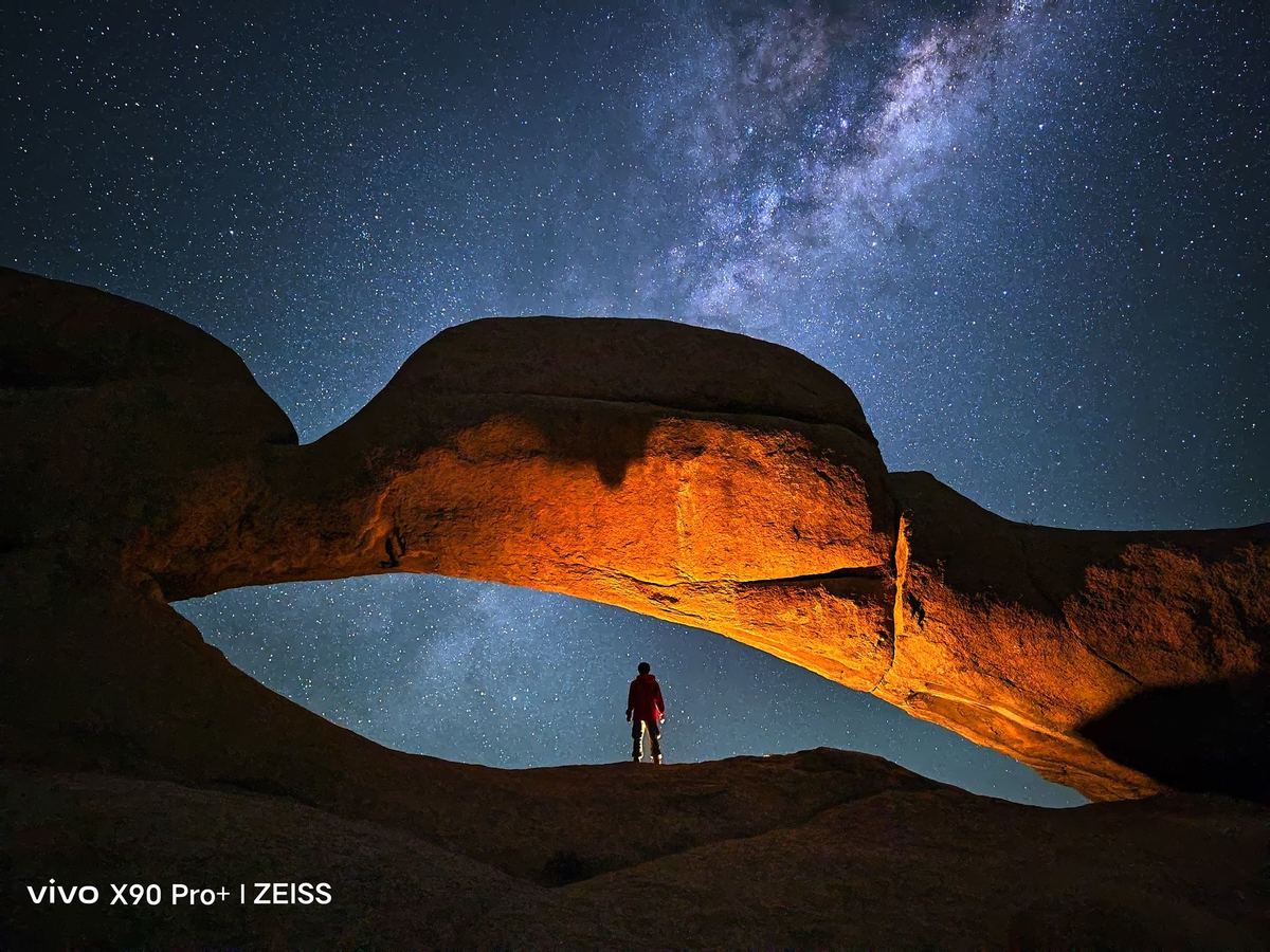 一个站在沙漠中的拱门下仰望夜空中星星的男子