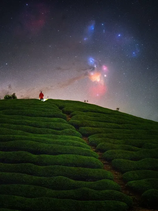 一个人在夜晚的绿色小山上 灯塔照亮了天空。