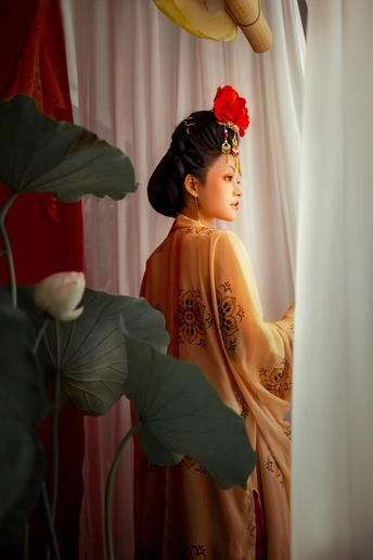 一位身穿橙色套装的年轻女士站在一朵红花旁边