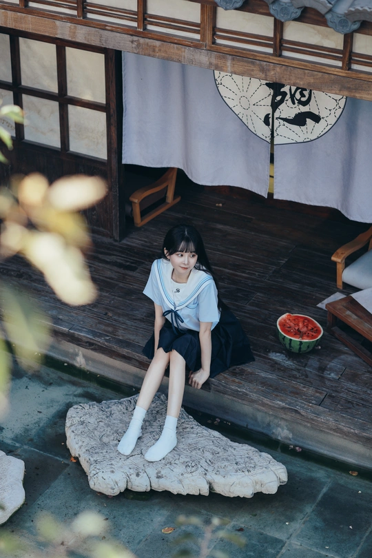 一个小女孩坐在房子前面的岩石上 地板上放着一个洋娃娃