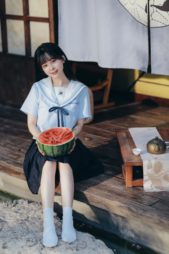 一位拿着一碗西瓜的年轻女士坐在外面