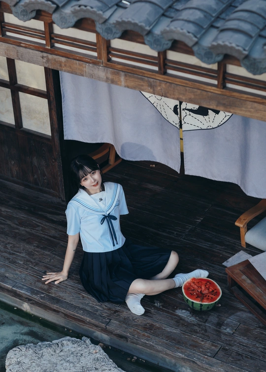 一个年轻的女人拿着一碗西瓜坐在木屋的地板上