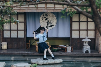 一个年轻女孩站在池塘前的岩石上 池塘的背景是一座建筑