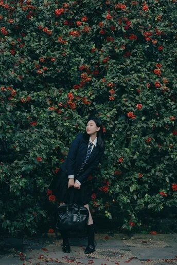一位穿着黑色外套的女士站在一棵开红花的树前