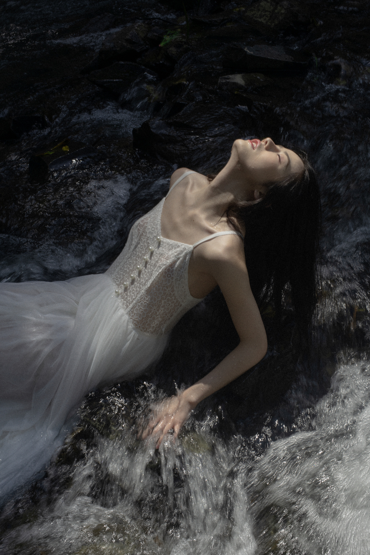 穿着白色连衣裙的美女躺在河里或小溪里的岩石上
