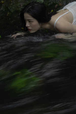 一个穿着白色连衣裙的女人躺在小溪里