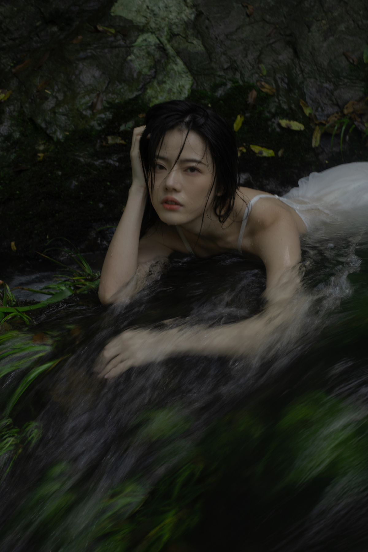 一个穿着白色连衣裙的年轻女子躺在溪流中