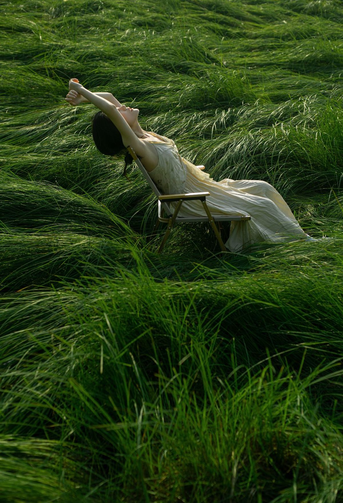 一个穿着长裙的女人躺在一片高高的绿色草地上