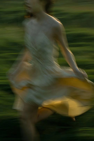 一位穿着黄裙子的年轻女子穿过一片绿色田野的模糊图像